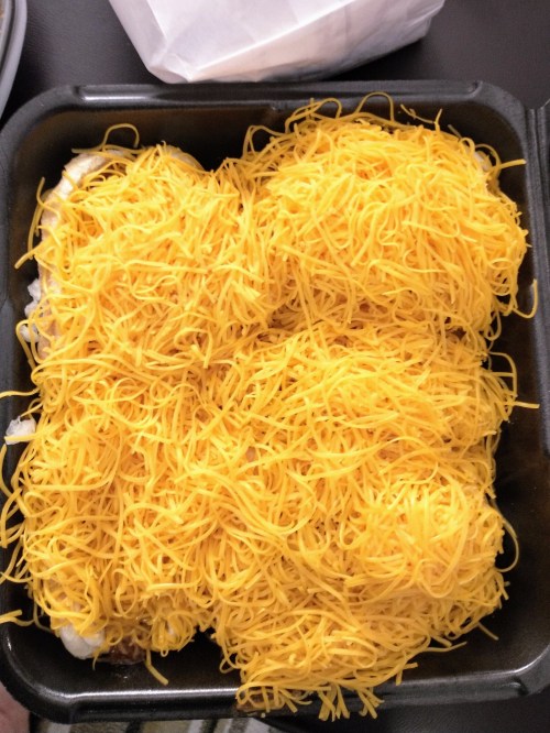 A takeout container filled with a generous layer of shredded yellow cheese over a dish.