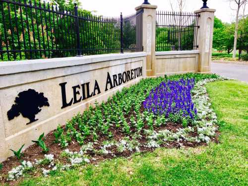 A stone sign reading "Leila Arboretum" surrounded by colorful flower beds and greenery.