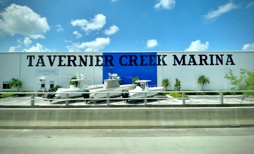 Sign for Tavernier Creek Marina with boats in front, under a bright blue sky.