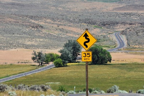 A winding road sign with a speed limit of 35 MPH, set against a backdrop of rolling hills and sparse vegetation.