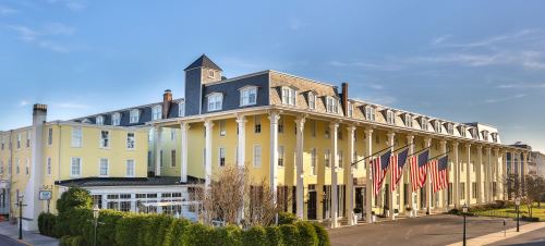 Historic yellow hotel with white columns and multiple American flags in front, set against a clear blue sky.