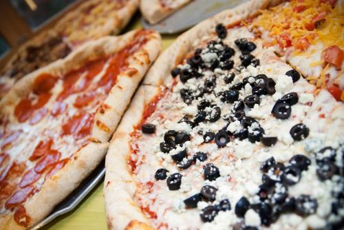 A variety of pizzas with toppings like pepperoni, cheese, tomatoes, and black olives on a table.