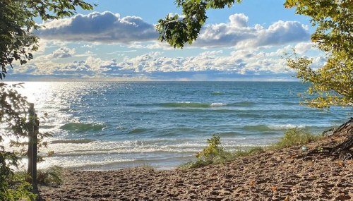 A serene beach scene with gentle waves, sandy shore, and a bright sky filled with clouds reflecting sunlight.