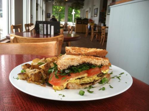 A hearty sandwich with eggs, tomatoes, and greens, served with seasoned potato wedges on a white plate.