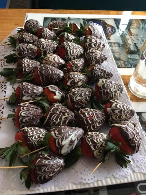 A platter of chocolate-covered strawberries with decorative white chocolate swirls, arranged neatly on a table.