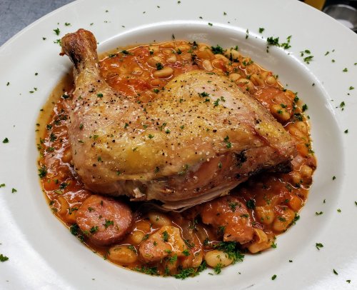 A plated chicken leg on a bed of beans in a savory sauce, garnished with parsley.