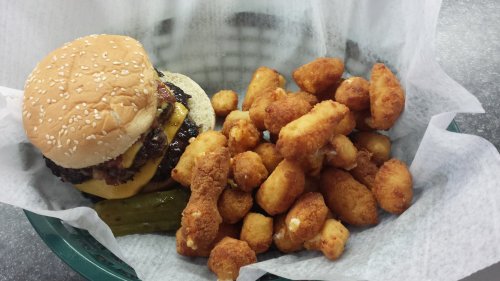A sesame seed bun burger with cheese and pickles, served with a side of golden, crispy tater tots in a basket.