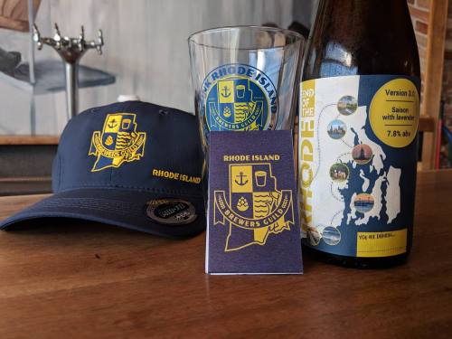 A navy cap, a glass, a beer bottle, and a booklet, all featuring the Rhode Island Brewers Guild logo.