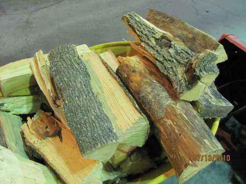 A pile of assorted firewood logs in a yellow container, featuring both bark-covered and smooth-cut pieces.