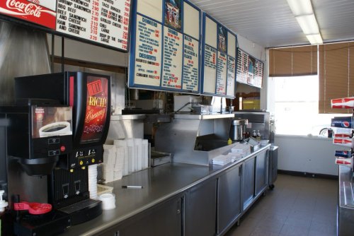 A diner interior featuring a menu board, drink dispenser, and stainless steel counter with food preparation areas.