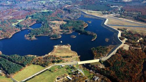 Aerial view of a winding lake surrounded by forests and fields, with a small community visible in the foreground.