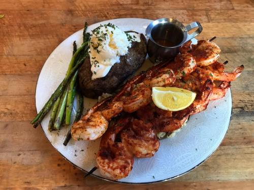A plate featuring grilled shrimp skewers, a baked potato with sour cream, asparagus, and a lemon wedge.