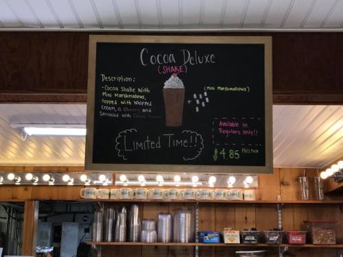 Chalkboard menu for "Cocoa Deluxe" shake, featuring mini marshmallows, whipped cream, and a cherry. Limited time offer.