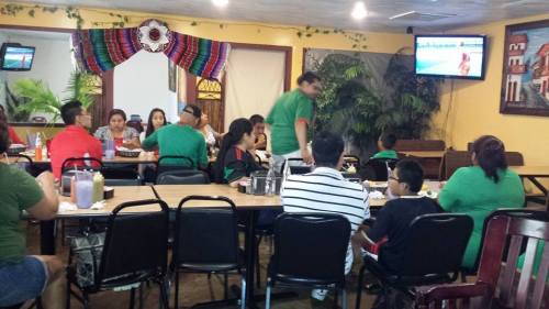 A lively restaurant scene with families dining, watching TV, and enjoying a meal together in a colorful setting.