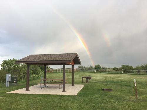 A picnic shelter on a grassy field with a rainbow in the background under a cloudy sky.