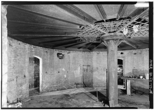 Interior of a circular, brick-walled room with a central column and a domed ceiling, featuring industrial elements.
