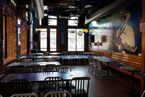 A cozy restaurant interior with wooden benches, tables, and a mural on the wall, featuring a stage for live performances.