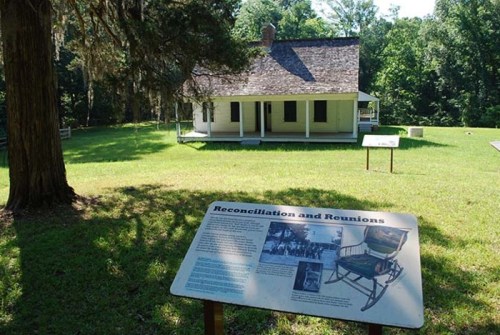 A historic house surrounded by trees, with an informational sign about reconciliations and reunions in the foreground.
