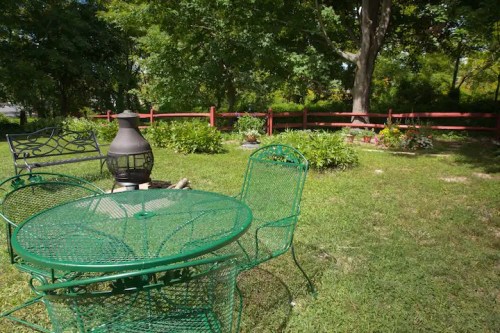 A green metal table and chairs in a garden, surrounded by trees and a red wooden fence.
