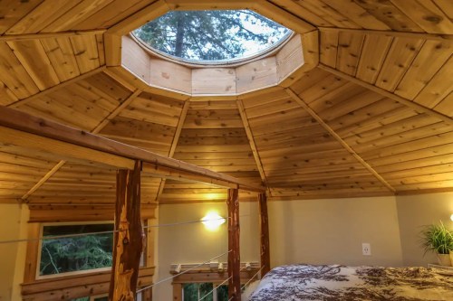 Cozy wooden interior of a cabin with a skylight, featuring a lofted bed and natural wood beams.