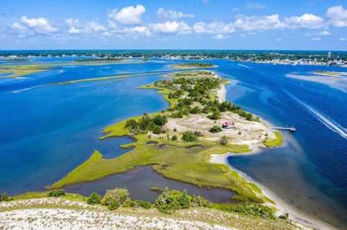 Aerial view of a coastal landscape featuring an island, waterways, and lush greenery under a bright blue sky.