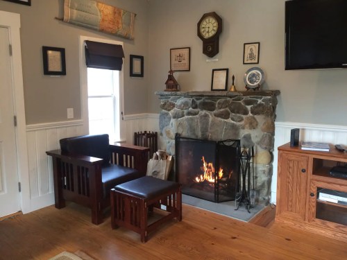 Cozy living room with a stone fireplace, wooden furniture, and wall decor, creating a warm atmosphere.