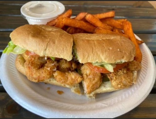 A plate with two fried chicken sandwiches topped with lettuce and tomato, served with sweet potato fries and a dipping sauce.