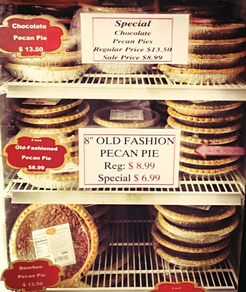 Display case filled with various pecan pies, featuring prices and special offers for chocolate and old-fashioned varieties.