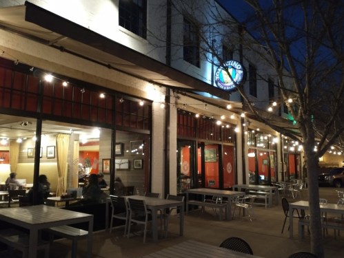 A cozy café exterior at night, featuring string lights, outdoor seating, and warm interior lighting visible through the windows.