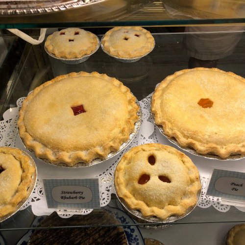 A display of three pies: a large strawberry rhubarb pie and two smaller peach pies, all with golden crusts.