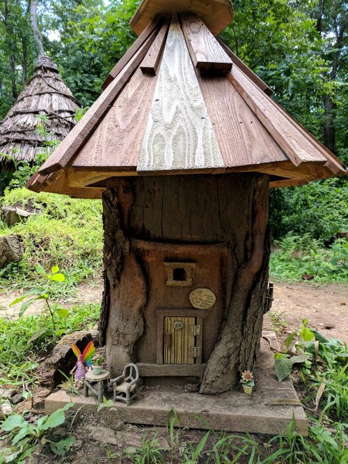 A whimsical treehouse with a wooden roof, surrounded by greenery and small decorative figures.