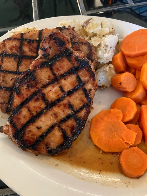 Grilled pork chops with a side of mashed potatoes and sliced carrots on a white plate.