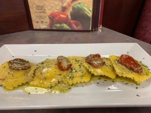 Plate of ravioli topped with sun-dried tomatoes and a creamy sauce, garnished with herbs.