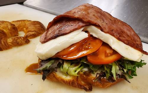 A croissant sandwich filled with lettuce, tomato, mozzarella, and slices of ham, resting on a cutting board.