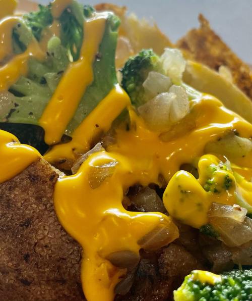 Close-up of a cheesy dish topped with broccoli and onions, featuring melted yellow cheese over a crispy base.
