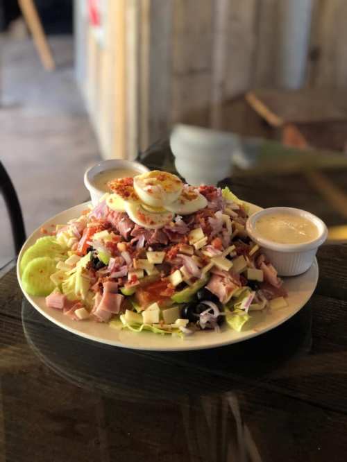 A large salad topped with sliced eggs, ham, cheese, and olives, served with two dressings on the side.