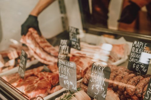 A display case filled with various cuts of pork, including ribs and sausages, with price tags visible.