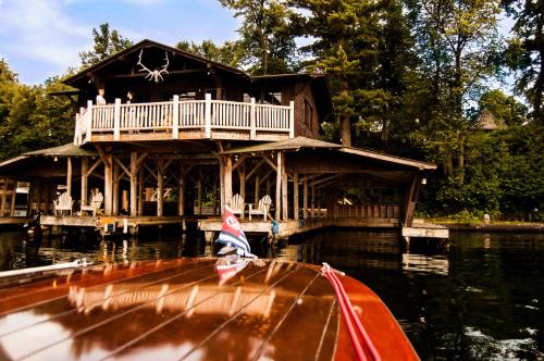 A wooden boathouse with a balcony, surrounded by trees, viewed from a boat on calm water.