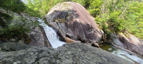 A rocky landscape with a waterfall cascading over boulders, surrounded by lush green trees.