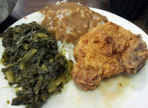 A plate of food featuring fried chicken, rice with brown gravy, and collard greens.