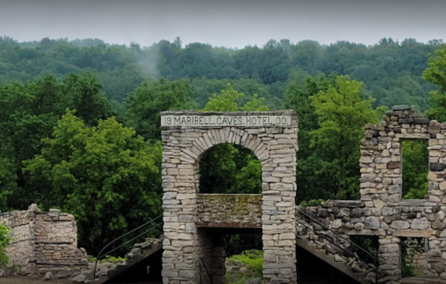 Ruins of the Maribell Caves Hotel, with stone archway and lush green trees in the background.