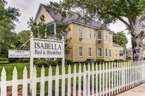 A charming yellow bed and breakfast with a white picket fence and a sign reading "Isabella Bed & Breakfast."