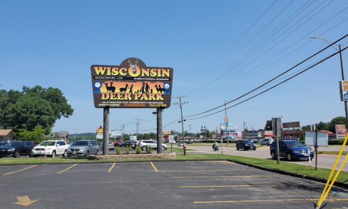 Sign for Wisconsin Deer Park with clear blue sky and vehicles parked in the foreground.