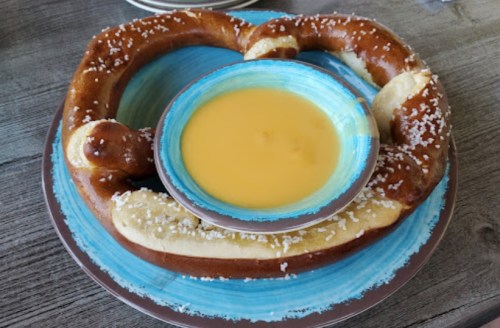 A large pretzel on a blue plate, served with a bowl of cheese dip in the center.
