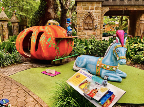A whimsical scene featuring a large orange pumpkin carriage and a blue horse statue in a lush garden setting.