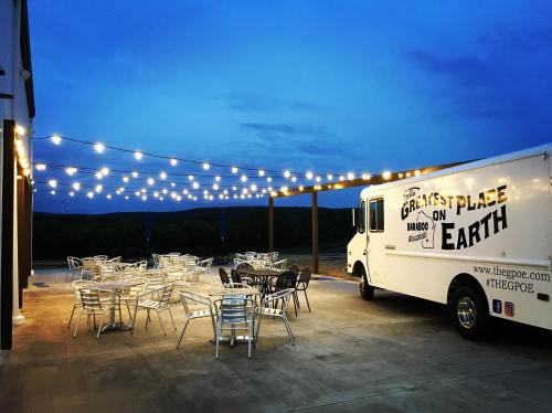 A food truck parked near outdoor seating under string lights at dusk, with a scenic view in the background.