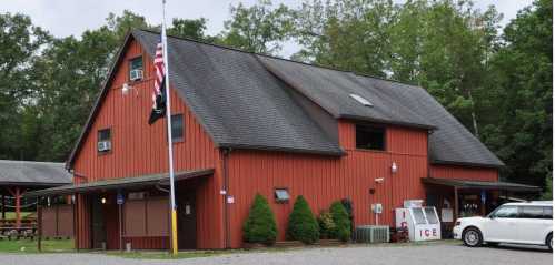 A red barn-style building surrounded by trees, featuring a flagpole and an ice vending machine outside.