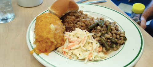 A plate of food featuring cornbread, coleslaw, green beans, black-eyed peas, and a serving of grain.