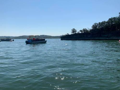 A calm lake scene with a boat and rocky shoreline under a clear blue sky.