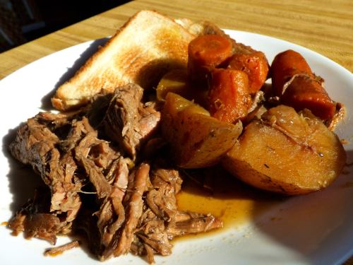 A plate of tender shredded beef with carrots and potatoes, served with a slice of toasted bread.